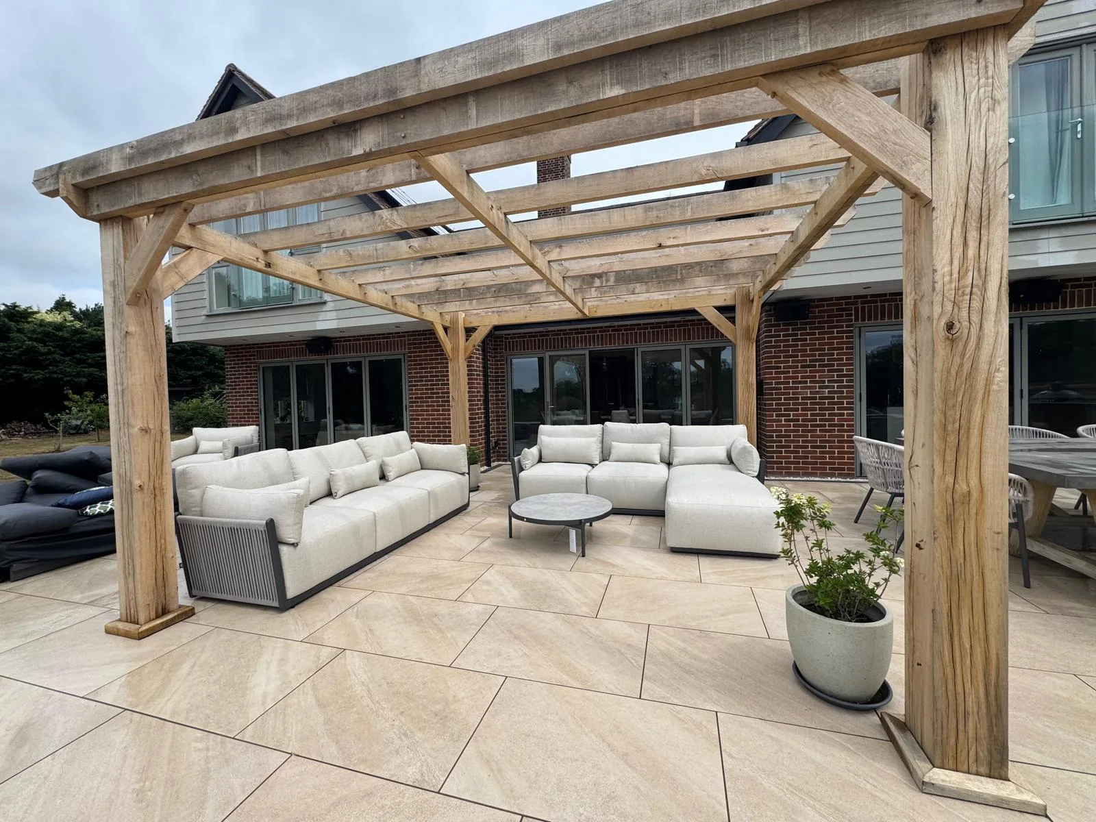 Cream porcelain patio and oak pergola with outdoor sofas at an Essex home