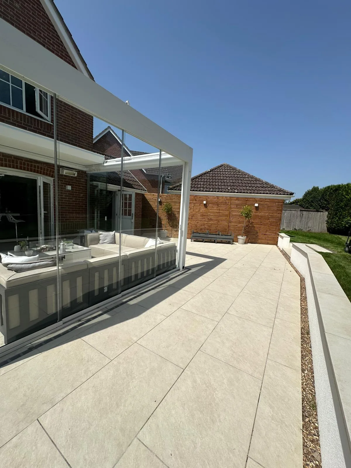 Cream porcelain patio and glass veranda with a gravel border in an Essex garden