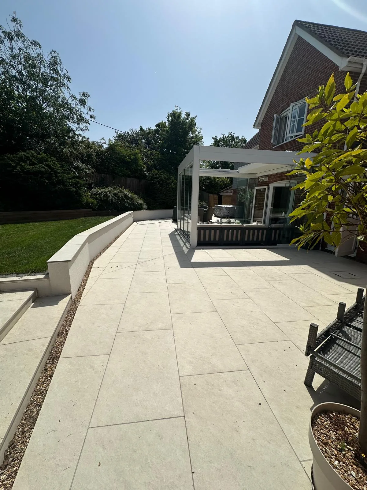 Wide cream porcelain patio with a white veranda and rendered retaining wall in Essex