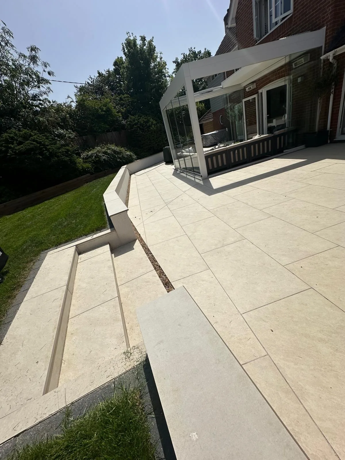 Cream porcelain patio with steps and a retaining wall by a glass veranda in Essex